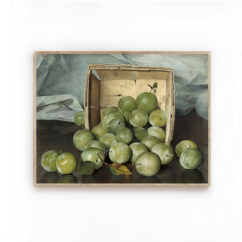 Op de afbeelding: Een stilleven met een houten mand vol groene pruimen. De pruimen vallen uit de mand op een donker oppervlak. De mand staat op een witte doek.