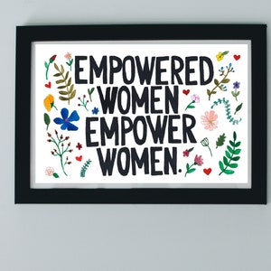 Może przedstawiać: Czarno-biały wydruk w ramie z tekstem "Empowered Women Empower Women." Wydruk jest otoczony kolorowymi kwiatami i liśćmi.
