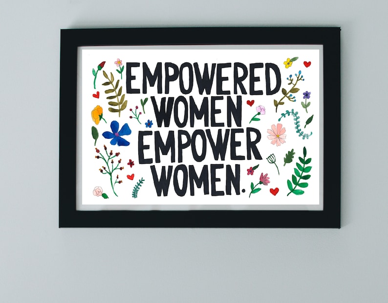 Może przedstawiać: Czarno-biały wydruk w ramie z tekstem "Empowered Women Empower Women." Wydruk jest otoczony kolorowymi kwiatami i liśćmi.