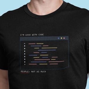 May include: Black t-shirt with a white text overlay that reads "I'm good with code" and a stylized image of a computer code window with colorful lines of code. Below the code window is the text "People, not as much."