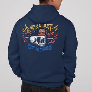 May include: Navy blue hoodie with a graphic on the back featuring a skull wearing a San Diego hat. The text reads "We're Just San Diego, Stay Classy, Getting Started" in a colorful design.