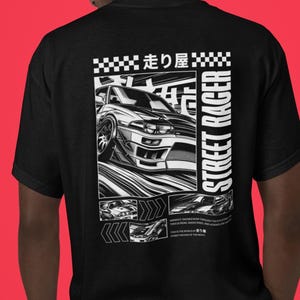 May include: Black t-shirt featuring a detailed black and white graphic of a sports car with the text "STREET RACER" and Japanese text. The design includes racing-themed elements.