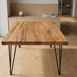 Könnte beinhalten: Ein rechteckiger Couchtisch mit einer dicken, naturbelassenen Tischplatte aus hellbraunem Holz mit sichtbarer Maserung und Astlöchern. Der Tisch wird von vier schlanken, schwarzen Haarnadelbeinen aus Metall getragen, die für Stabilität sorgen.