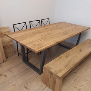 Peut inclure: Une table à manger en bois avec un cadre en métal noir et un banc en bois assorti. La table a une finition en bois naturel et le banc a une finition légèrement plus foncée. Il y a trois chaises en métal noir avec un dossier en forme de croix.