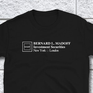 May include: Black t-shirt with white text that reads "BERNARD L. MADOFF Investment Securities New York  London" and a small square with the text "MADOFF" inside.