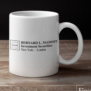 May include: White ceramic coffee mug with a black logo that reads "BERNARD L. MADOFF Investment Securities New York  London" with a small square logo that reads "MADE" in the top left corner.