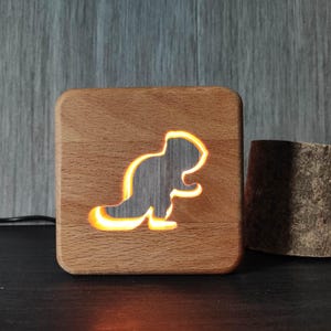 May include: A wooden night light with a cutout of a beaver. The light is on and the beaver is illuminated.