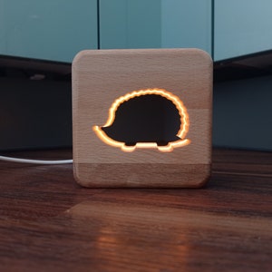 Könnte beinhalten: Ein hölzernes Nachtlicht in Form eines Igels mit einem ausgeschnittenen Design. Das Licht ist an und beleuchtet die Igelform.