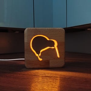 Puede incluir: Una luz nocturna de madera con forma de kiwi con un brillo amarillo cálido.