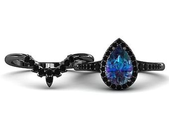 May include: A black engagement ring set featuring a pear-shaped, color-changing gemstone with a halo of black stones. The set includes a matching curved band, all set against a white background.