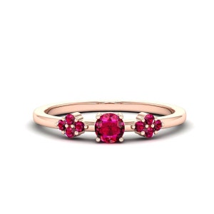 May include: A rose gold ring with three clusters of ruby red gemstones. The center cluster features a larger round gemstone, while the two side clusters feature smaller round gemstones.