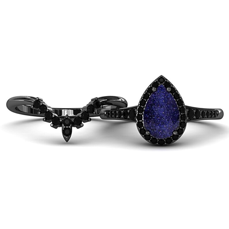 May include: A black ring set featuring a pear-shaped blue gemstone with a black halo and a matching curved band. The rings have a dark, metallic finish and are set against a white background.