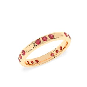 May include: A gold ring with a continuous row of small, round, red gemstones. The ring has a smooth, polished surface and a classic design. The gemstones are evenly spaced around the band.