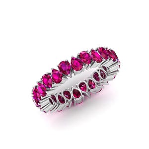 Puede incluir: Un anillo de plata con una fila continua de gemas fucsia en forma de pera. El diseño del anillo muestra las gemas muy juntas, creando una banda completa de color y brillo. El anillo está sobre un fondo blanco.