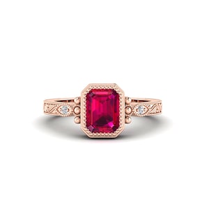 Puede incluir: Anillo de oro rosa con una gran gema roja brillante de forma rectangular. El anillo tiene un diseño ornamentado con pequeñas piedras de acento y bordes con cuentas. La banda tiene un patrón grabado. Una hermosa joya.