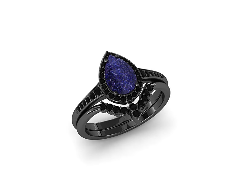 May include: A black ring set featuring a pear-shaped blue gemstone with a sparkling appearance, surrounded by small black stones. The set includes a matching band with additional black stones, creating a cohesive and elegant design.