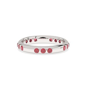 May include: A silver ring with a continuous row of round, red gemstones. The gemstones are evenly spaced around the band. The ring is set against a white background.