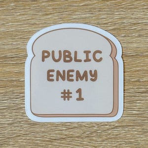 May include: A white sticker shaped like a slice of bread with the text "PUBLIC ENEMY #1" in brown lettering.