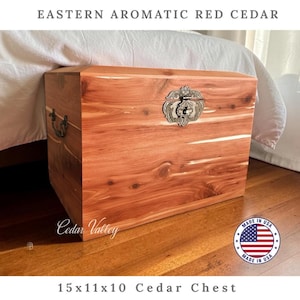 May include: A rectangular Eastern Aromatic Red Cedar chest measuring 15x11x10 inches. The wooden storage box features a natural reddish-brown grain, a decorative silver-toned metal latch on the front, and matching metal side handles.