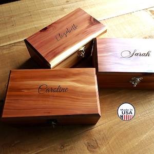 May include: Three rectangular wooden boxes with hinged lids and metal latches. Each box features a natural reddish-brown wood grain and is engraved with a name: Elizabeth, Sarah, or Caroline. A circular sticker reads Made in USA.