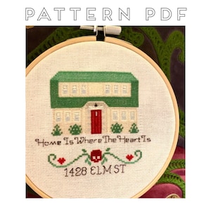 May include: Cross-stitch pattern in a wooden hoop featuring a house with a green roof and red door. The text "Home Is Where The Heart Is" and "1428 ELM ST" are stitched below the house. The words "PATTERN PDF" are at the top.