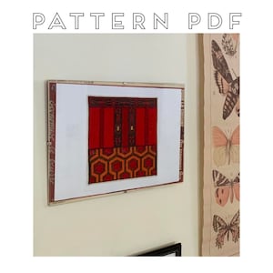 May include: A framed cross-stitch pattern of the iconic red carpet and doors from the movie "The Shining". The pattern features a red carpet with a black and white geometric design.
