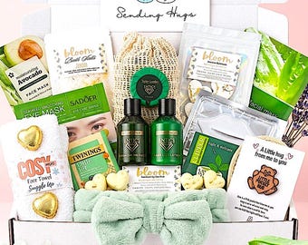 Könnte beinhalten: Eine weiße Geschenkbox mit der Aufschrift Sending Hugs enthält verschiedene Pflegeprodukte wie Gesichtsmasken, Badesalz, zwei grüne Lotionsflaschen, ein weißes Handtuch mit goldenen Herzen, ein hellgrünes Schleifen-Stirnband, Tee und einen Bären.