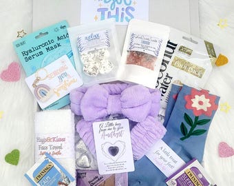 Può includere: Una confezione regalo con articoli per la cura di sé. Include una fascia viola, una maschera per il viso, sali da bagno, calzini con un motivo floreale, bustine di tè, un portachiavi e una carta con la scritta "You got this".