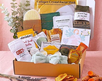 Puede incluir: Una caja de regalo llena de artículos de cuidado personal, que incluyen una mascarilla facial, calcetines con el texto "Warm hugs for the feet!", una diadema y té. La caja contiene una variedad de productos para la relajación y el bienestar.