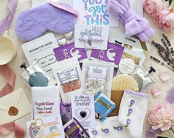 May include: A gift box filled with self-care items in shades of purple and white. Includes a sleep mask, headband, face masks, bath salts, tea, socks, and a keychain with the text "Sending you sunshine". The box also contains a card that says "You got this".