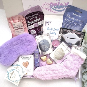 Könnte beinhalten: Eine violette und weiße Geschenkbox für die Selbstpflege, gefüllt mit lavendel-duftenden Badeprodukten, einer flauschigen Augenmaske und einem Paar flauschiger Socken. Die Box enthält eine rosa Tonerde-Gesichtsmaske, Fußbadsalze, eine selbstwärmende Augenmaske, eine Lippenmaske und ein Lavendelöl zum Auftragen.