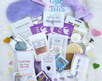 May include: A gift box filled with self-care items. Includes a lavender eye mask, face masks, bath salts, a bracelet, a headband, a face towel, socks, tea bags, and a keychain. The box contains cards with the phrases "You got this", "Hello gorgeous", and "Sending you sunshine".
