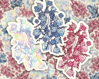 May include: Three stickers featuring a sword design adorned with dice and flowers. One sticker has a rainbow holographic effect, another is blue, and the third is pink. The stickers are on a floral background.