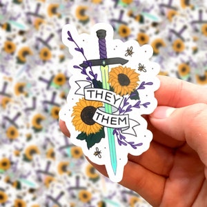 Könnte beinhalten: Ein Aufkleber mit einem Schwert mit lila Knauf und grüner Klinge, verziert mit Sonnenblumen und Lavendelzweigen. Die Worte "THEY THEM" sind auf einem Banner zu sehen. Kleine Bienen sind ebenfalls im Design enthalten.