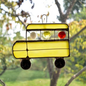 May include: A yellow stained glass school bus with three round windows. The windows are filled with white, yellow, and red glass.