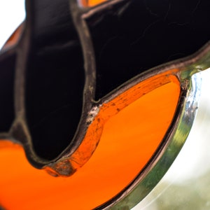 May include: Close-up of a stained glass piece with a black and orange design. The orange glass is shaped like a crescent moon and is surrounded by black glass.