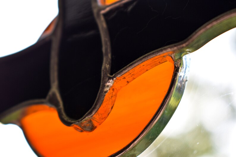 May include: Close-up of a stained glass piece with a black and orange design. The orange glass is shaped like a crescent moon and is surrounded by black glass.