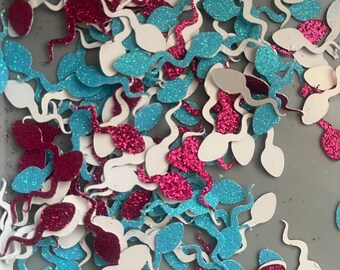 Könnte beinhalten: Eine Ansammlung von glitzernden, spermaförmigen Konfetti in Weiß, Türkis und Magenta. Das Konfetti ist auf einer grauen Oberfläche verstreut und erzeugt ein verspieltes und festliches Aussehen. Die Formen sind detailliert und haben ein funkelndes Finish.