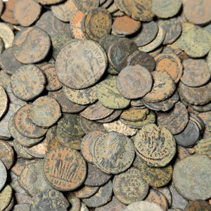 May include: A large collection of ancient Roman bronze coins. The coins are in various states of wear and tear, with some showing signs of corrosion. The coins are arranged in a random pattern, with some overlapping.