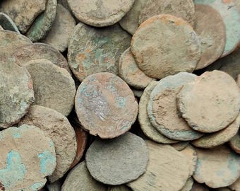 Op de afbeelding: Een close-up van een verzameling antieke, bronskleurige munten. De ronde munten hebben een ruw, getextureerd oppervlak met groene en blauwe oxidatie. De afbeelding suggereert een historisch thema.