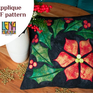 May include: A black pillow with an applique design of a poinsettia and holly leaves. The poinsettia is red with gold accents and the holly leaves are green with gold accents. The pillow is on a wooden table with a white vase and gold snowflakes.
