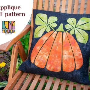 May include: A black pillow with an orange pumpkin applique and green leaves. The pillow is sitting on a wooden chair in a garden setting. The text "Lena Pugachova Quilt Art" is visible in the upper left corner of the image.