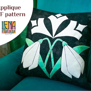 Op de afbeelding: Een zwart-wit kussen met een appliqué-ontwerp van witte sneeuwklokjes op een groene stengel. Het kussen ligt op een turquoise bank. De tekst "Applique PDF pattern" staat in de linkerbovenhoek van de afbeelding. De tekst "Lena Pugachova Quilt Art" staat in de linkerbenedenhoek van de afbeelding.