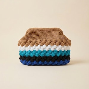 May include: A handmade crochet clutch in a variety of colors. The top is a solid brown, followed by white, blue, black, and blue rows. The clutch has a textured, bobble stitch design.