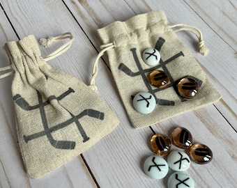 May include: Two small beige fabric bags with black hockey stick designs and white and brown glass game pieces with black hockey stick designs.