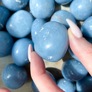 May include: A collection of smooth, light blue tumbled stones. The stones are various sizes and shapes, and some have a slightly cloudy appearance.