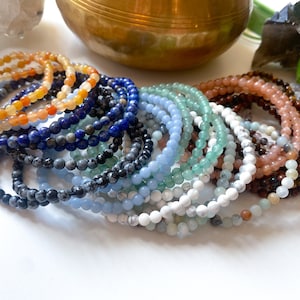May include: A collection of colourful gemstone bracelets, including blue lapis lazuli, green aventurine, white howlite, and orange carnelian. The bracelets are stacked on top of each other, creating a beautiful and vibrant display.