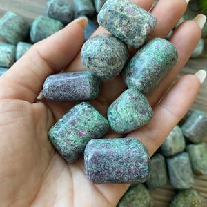 Könnte beinhalten: Eine Sammlung von polierten, grünen und rosafarbenen Rubin-Zoisit-Steinen. Die Steine sind glatt und poliert und haben verschiedene Größen und Formen.