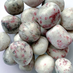 May include: A collection of tumbled stones with a white base and red and gray markings. The stones are smooth and polished.