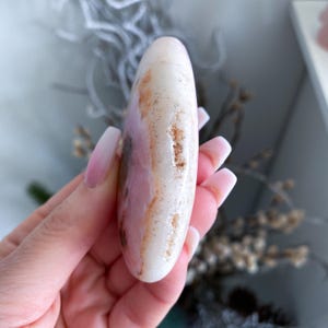 Hand holding a smooth, oval-shaped stone with a blurred natural background